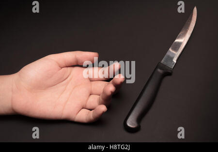 A sharp kitchen knife beside somebody's hand on dark background. This image was shot with single flash light bouncing technique. Stock Photo