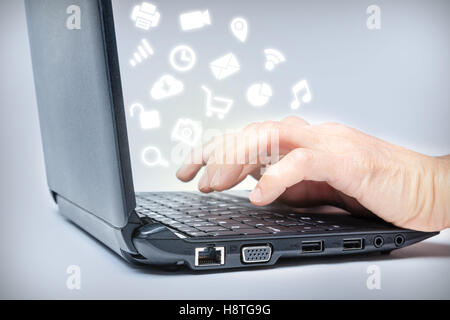 Hands typing on keyboard with common media icons rising from laptop. Multi-tasking on the Internet. Stock Photo