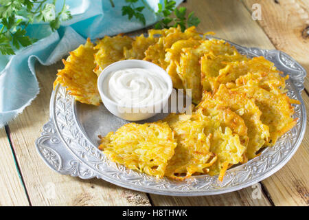 Homemade traditional potato pancakes, served with sour cream sauce. Hanukkah holiday meal on vintage wooden background. Stock Photo