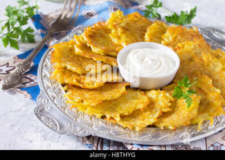 Homemade traditional potato pancakes, served with sour cream sauce, top view. Hanukkah holiday meal on vintage concrete backgrou Stock Photo