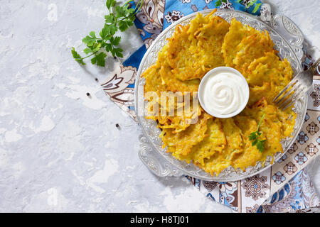 Homemade traditional potato pancakes, served with sour cream sauce, top view. Hanukkah holiday meal on vintage concrete backgrou Stock Photo