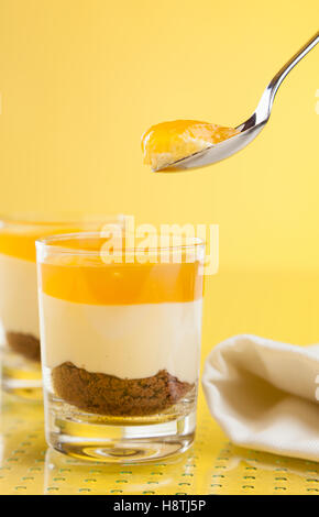 New York Cheesecake with mango topping in glasses and on spoon on yellow table Stock Photo