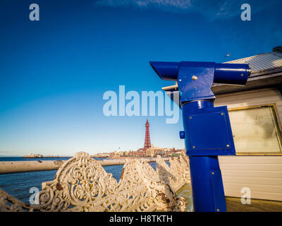 Traditional cast iron seats and Pay to View telescope on Pier, with Blackpool Tower in distance, Blackpool, Lancashire, UK. Stock Photo