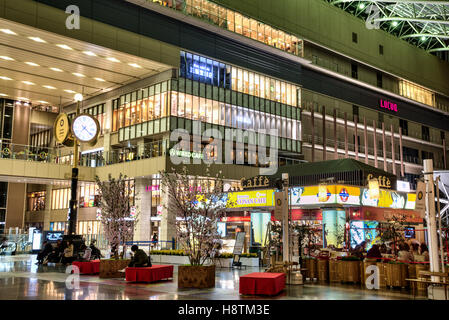 Japan, Osaka Station City interior. Taki-no-hiroba Plaza, with clock, cafe and North Gate Building entrance area with shops and stores. Night time. Stock Photo