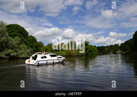 White motor boat cruising down the River Yare at Bramerton Woods End on the Norfolk Broads Stock Photo
