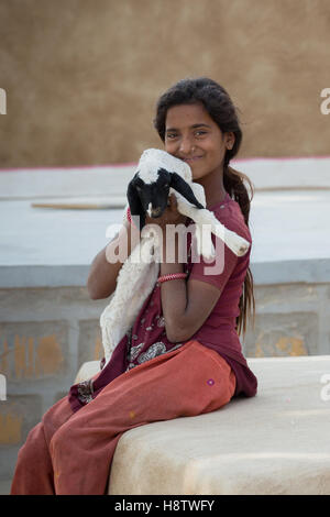 young Indian girl  sits in front of her house and hugs a baby lamb in rural areas of Jaisalmer, India Stock Photo