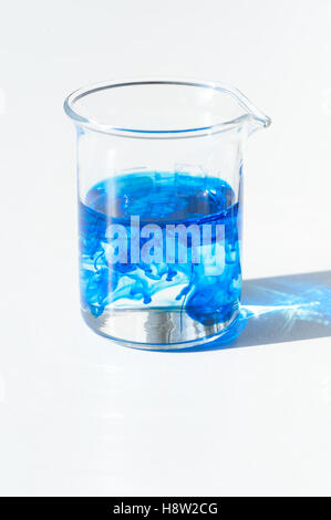 Chemistry lab measuring cup, beaker glass with blue food coloring solution to dissolve Stock Photo