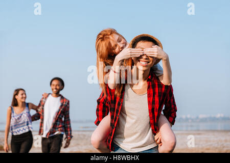 Happy redhead young woman covered eyes of her boyfriend by hands outdoors Stock Photo