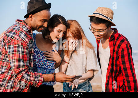 Multiethnic group of happy surprised young people using mobile phone together Stock Photo