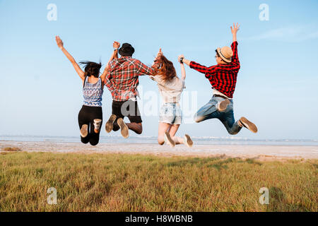 Back view of happy excited young people holding hands and jumping in the air outdoors Stock Photo