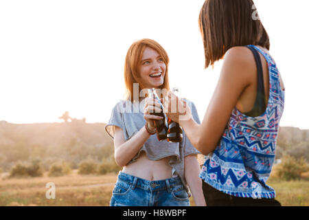 Two smiling young women standing and drinking soda outdoors Stock Photo