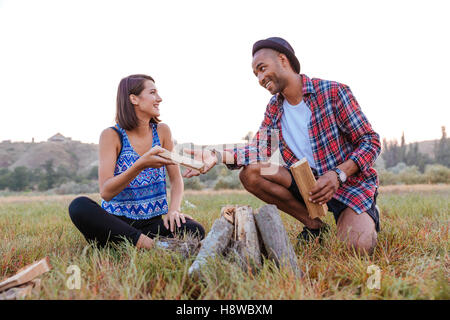 Cheerful young couple smiling and making campfire outdoors Stock Photo