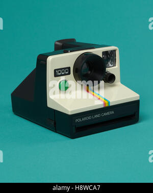 product shot of an iconic vintage polaroid 1000 land camera with green shutter button on sea green background. Stock Photo