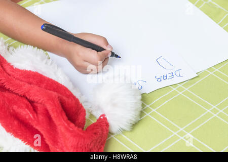 Children's hand is writing a letter to Santa Claus. On the table is Santa's cap. Stock Photo