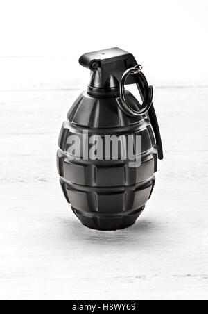 Grenade standing upright with the pin safely in position on a white wooden board in a close up view Stock Photo