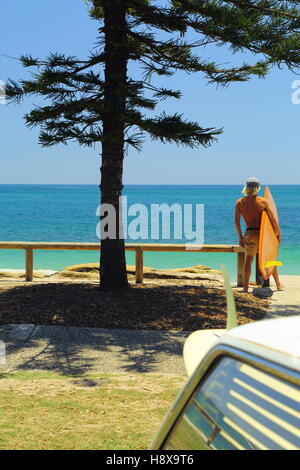 A blond haired man in his twenties holds his surfboard at Moffat Beach on the Sunshine Coast in Queensland, Australia. Stock Photo