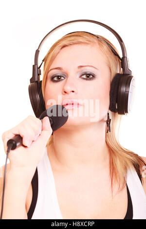 Music, passion concept. Studio shot of blonde young woman singing to microphone and wearing big headphones on her head, isolated portrait Stock Photo