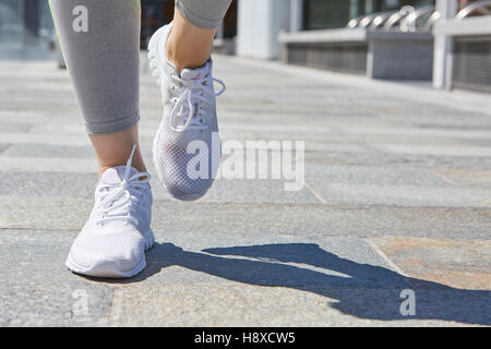 Woman running with white shoes outdoor in the city in a sunny day Stock Photo