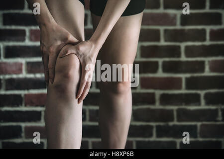 her knee feel painful after fitness exercise, healthy lifestyle concept, indoors gym wooden floor brick wall background Stock Photo