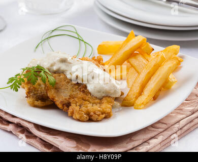 Breaded cutlet with blue cheese sauce and fried potatoes. Stock Photo