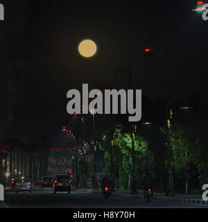 A full moon hangs over a busy avenue in Fès, Morocco, cars and street lamps tracing red and white light trails into the night. Stock Photo