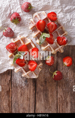 Belgian waffles with strawberries and powdered sugar close-up on the table. Vertical view from above Stock Photo