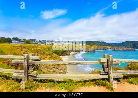 View through rustic wooden fence of sand beach below Main Street and houses of Mendocino town communinty on a sunny summer day Stock Photo