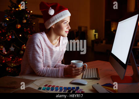 Woman in Santa cap networking on xmas night Stock Photo