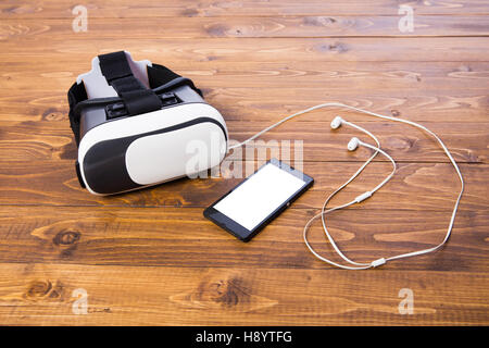 front side of a vr headset with earbuds and a smart phone, isolated on wooden floor background Stock Photo