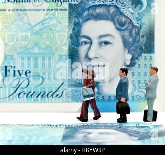 Miniature figurines walking in front of a five pound note. Stock Photo