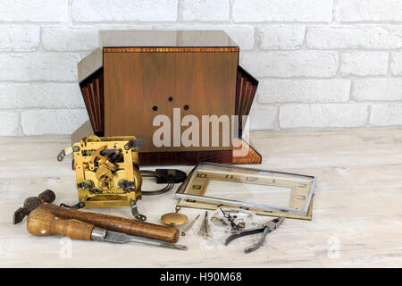 Vintage art deco wooden mantel clock in pieces with tools with old white brick wall effect background Stock Photo