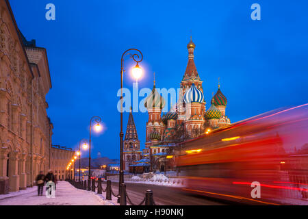 Red touristic bus passing by St. Basils Cathedral at dusk, Red Square, Moscow, Russia Stock Photo