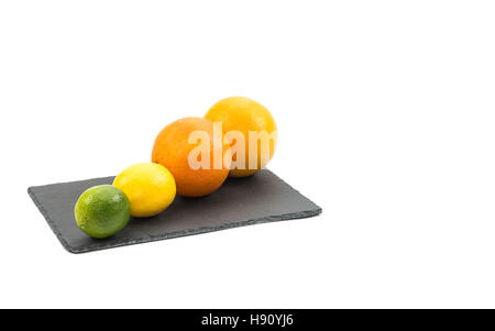 Whole citrus fruits, lime, lemon, grapefruit and orange on black slate board isolated on white Stock Photo