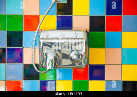 A metal hand dryer mounted on a colourful tiled wall. Stock Photo