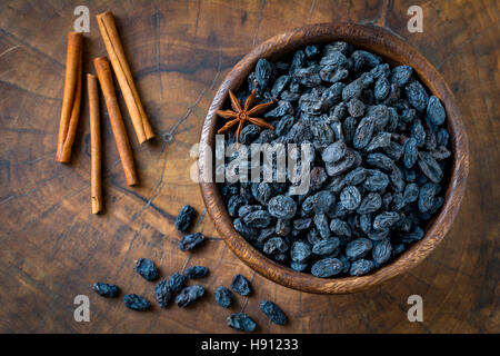 Black raisins and spices in wooden bowl. Top view, close up, horizontal Stock Photo