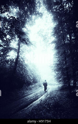 man walking on dark forest road on rainy day Stock Photo