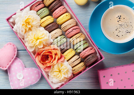 Colorful macaroons and coffee on wooden table. Sweet macarons in gift box and hearts. Top view Stock Photo