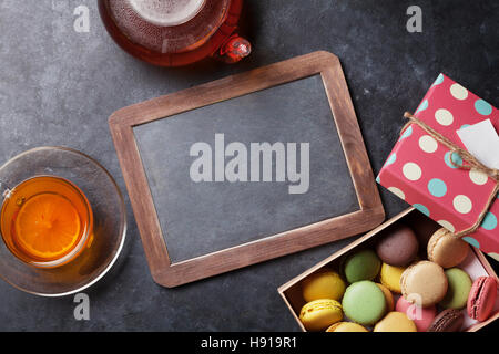 Tea cup, teapot, chalkboard and macaroons gift box on stone table. Top view with copy space Stock Photo