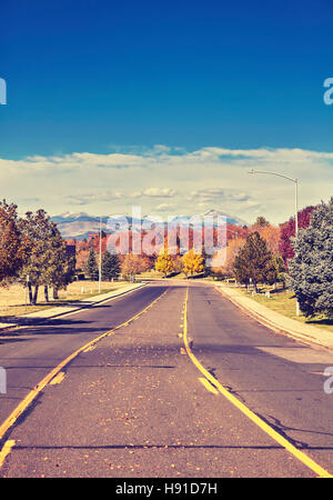 Retro stylized photo of an autumn road with Rocky Mountains in distance, Colorado, USA. Stock Photo
