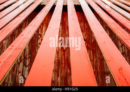 Fresh red painted wooden planks are drying near rural Norwegian barn, photo background with perspective effect and selective focus Stock Photo