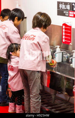 Japan, Nishinomiya, KidZania, Child's activity play park. Interior. Coke-Cola bottling store. Children washing hands under tap at sink. Stock Photo