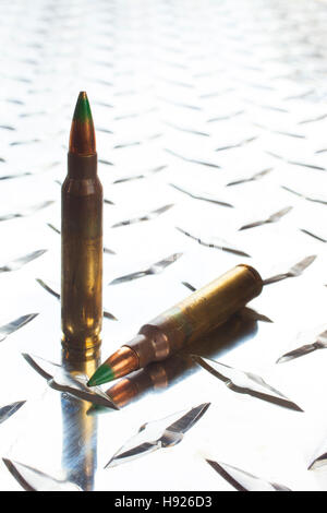 Rifle cartridges with green tipped bullets on a shiny piece of armor plate Stock Photo