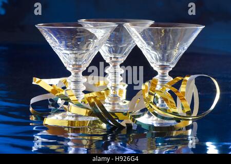 Three cocktail glasses with golden serpentine against blue background with reflection Stock Photo