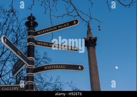 Sign post in trafalgar square at dusk with nelsons coloumn and full moon behind Stock Photo