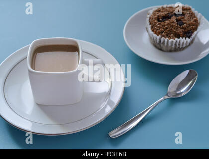 White square cup of coffee, silver spoon and brown fiber muffin set on blue table , viewed from slightly above Stock Photo