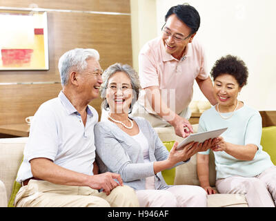 two active senior asian couples looking at tablet computer, happy and laughing Stock Photo