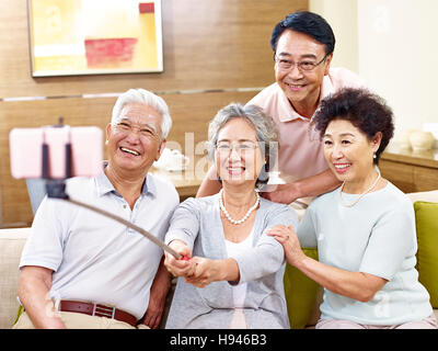two active senior asian couples taking a selfie using mobile phone on a selfie stick, happy and smiling