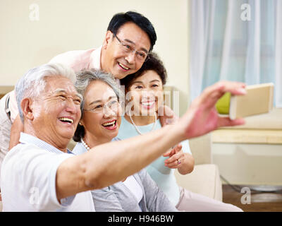 two active senior asian couples taking a selfie using mobile phone, happy and smiling