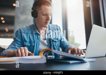 Indoor shot of male student studying in library at university. Young man using laptop and reading book with focus on hand. Stock Photo