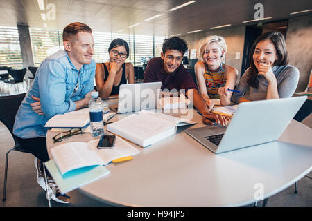 Multiethnic group of young people studying together at a table looking at laptop. Young students in cooperation with their school assignment. Stock Photo